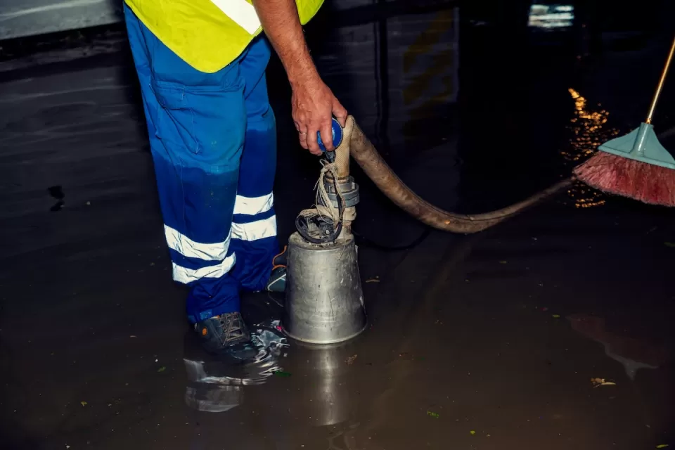 Worker in blue pants holding hose while standing in flooded interior room.